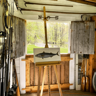 A fish painting on an easel with a creek in the background